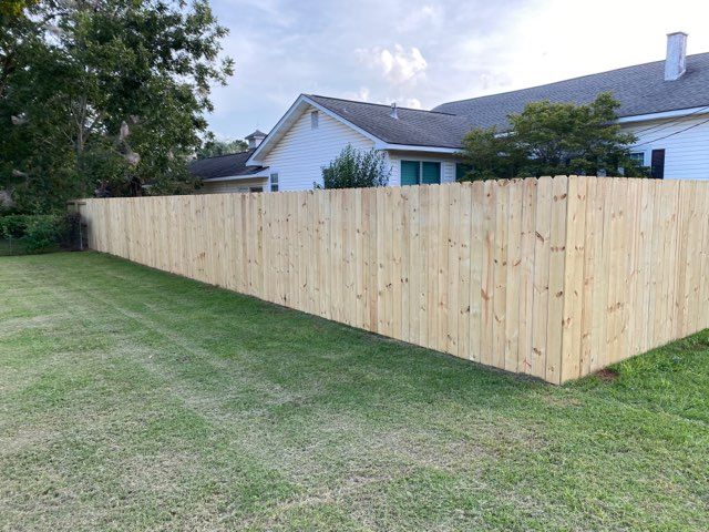 Wooden fence around a grassy yard, with a white house in the background.