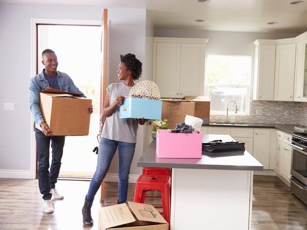 A couple carries cardboard boxes into a modern kitchen, smiling as they move into their new home.