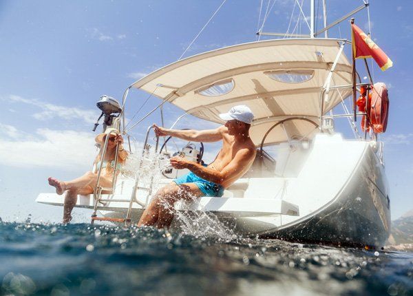 Recreation Vehicle — Charlotte, NC — AAC Insurance Group A person sits at the helm of a sailboat while another relaxes nearby, with the boat moving through sunny, blue ocean waters.