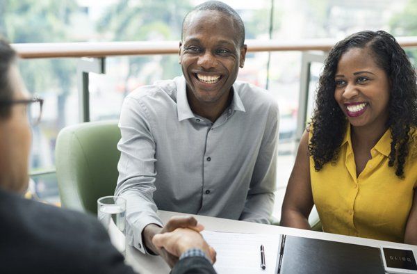 Business Communication — Charlotte, NC — AAC Insurance Group A professional shaking hands with a smiling couple across a table in a brightly lit office setting.
