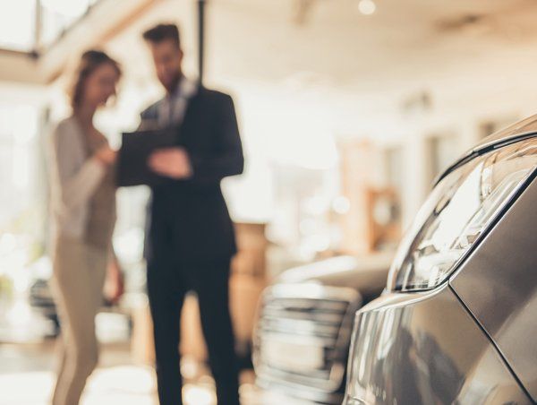 Car Insurance — Charlotte, NC — AAC Insurance Group A salesperson and a customer stand in a car dealership, viewing documentation near a vehicle.