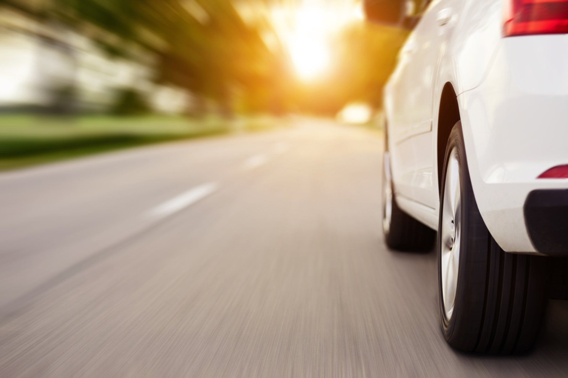 Happy Couple Sailing — Charlotte, NC — AAC Insurance Group A white car driving on a road at sunset, captured from a low, close-up angle of the rear wheel with motion blur.