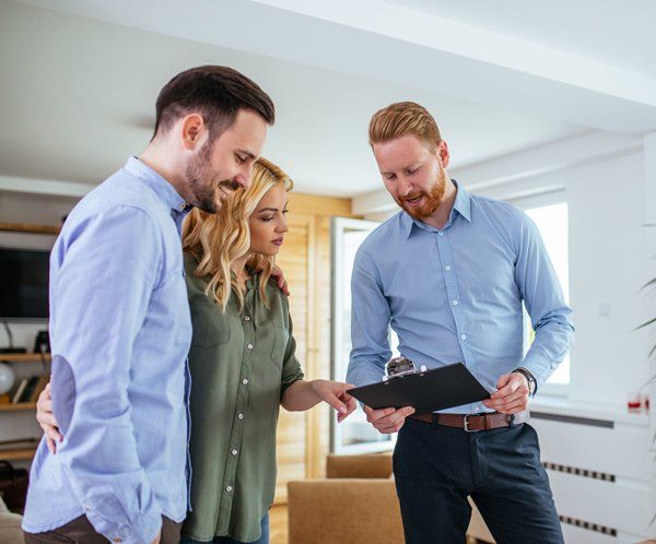 A professional discusses documents on a clipboard with a couple in a brightly lit, modern living space.