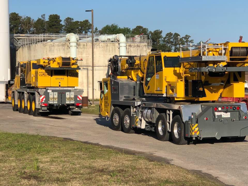 Two yellow heavy-duty cranes parked on a road near concrete structures and trees