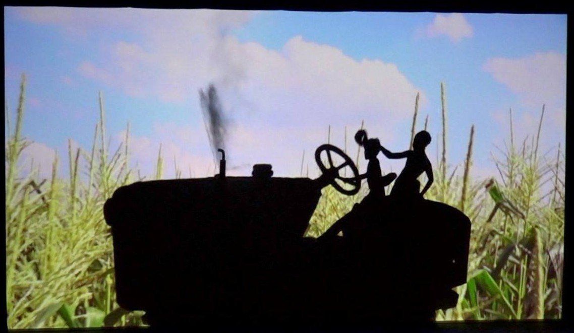 Silhouette of a tractor and driver in a field of tall grass at sunset