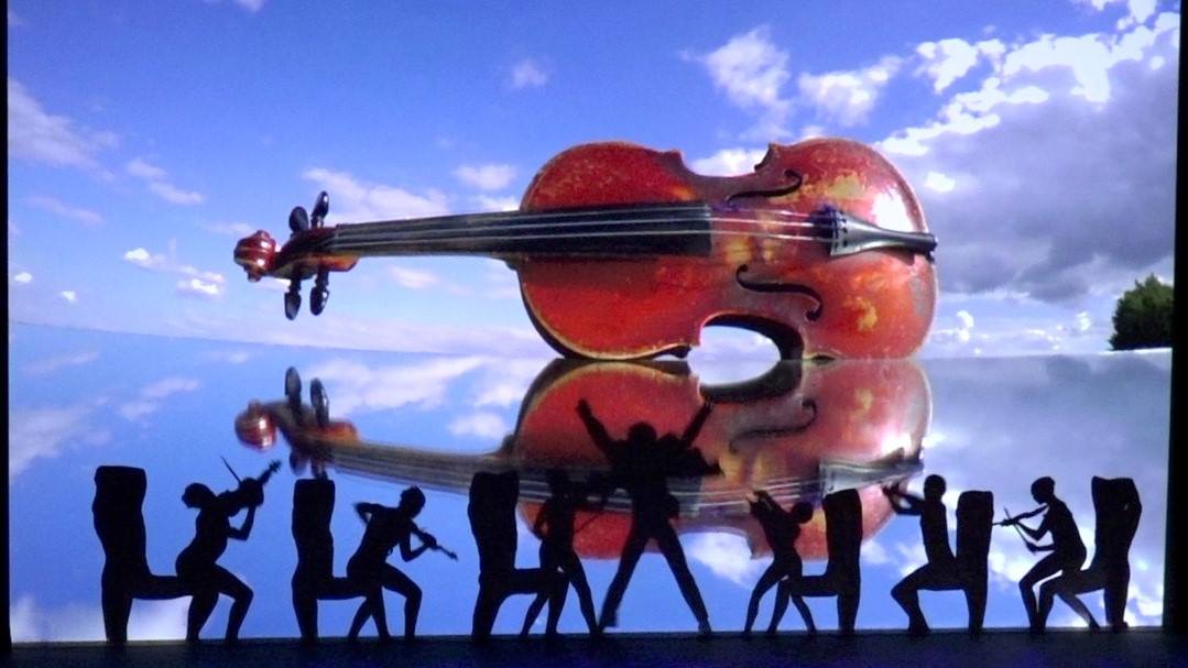 Silhouetted crowd dancing in front of a giant violin sculpture at sunset
