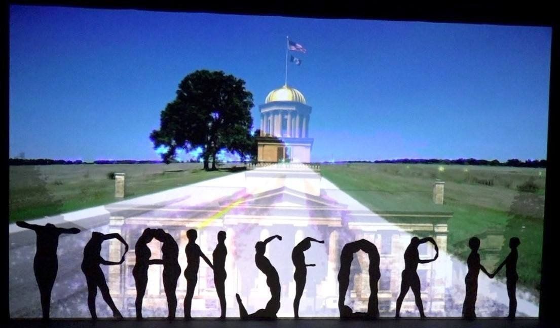 Protest sign reading “TRANSFORM” in front of a domed building and path under a blue sky