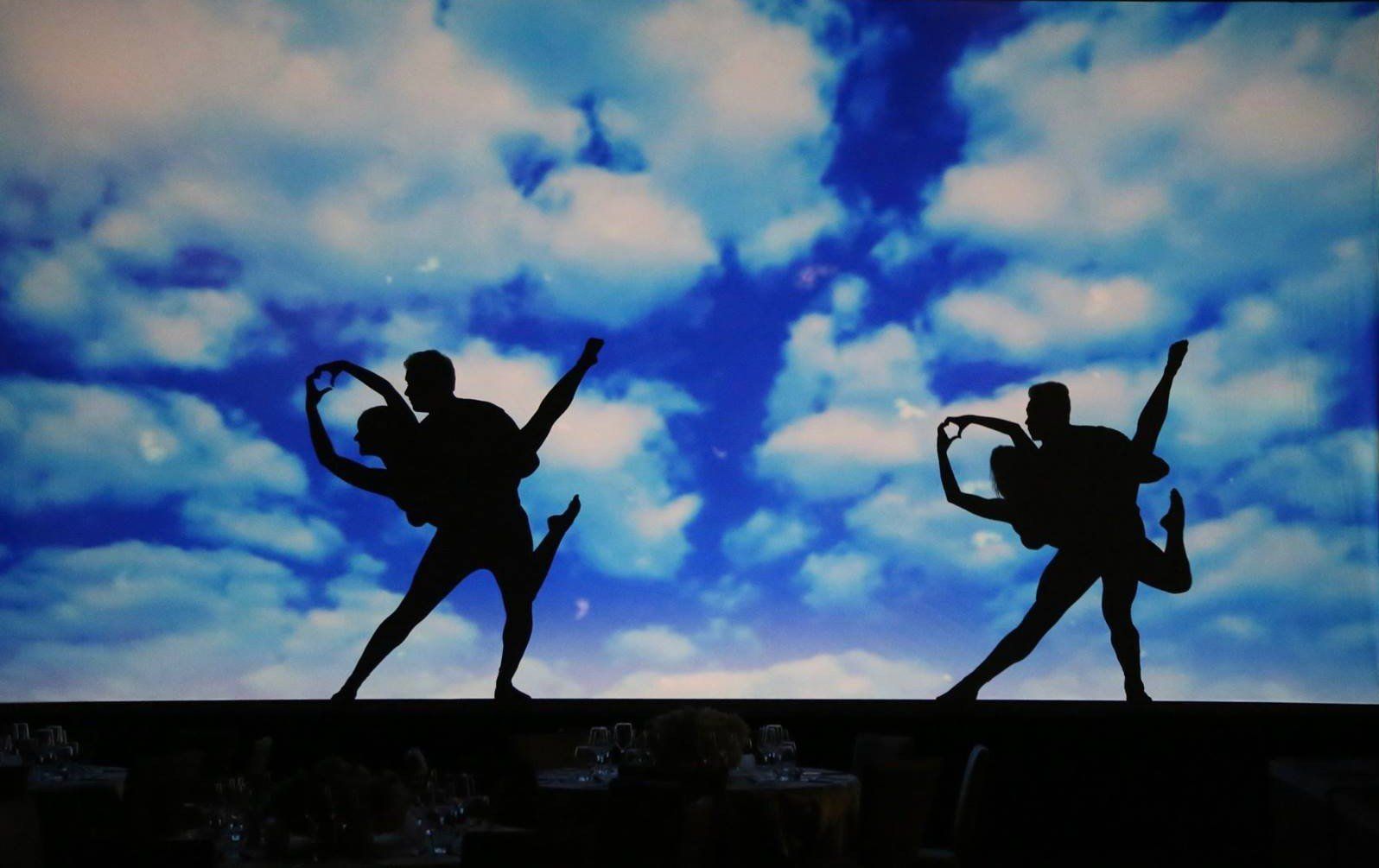 Two silhouetted dancers posing against a blue sky with clouds
