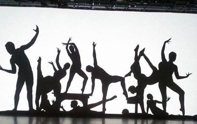 Black silhouettes of people dancing and posing in a line against a white background