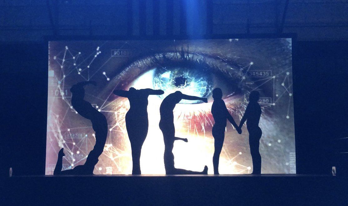 People silhouetted in front of large glowing letters spelling “STEM” on a dark stage.