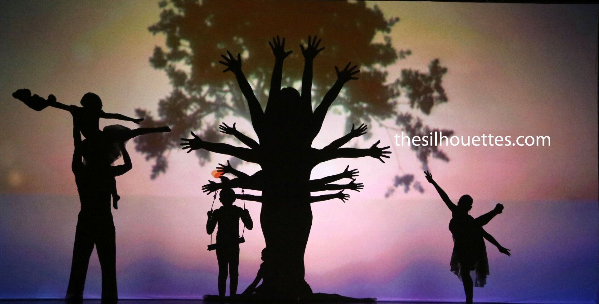 Silhouettes of children around a tree at sunset, with colorful pink and purple sky