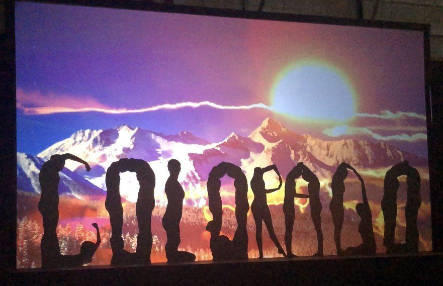 Silhouetted people in a line before a mountain sunset with a bright sun and purple sky
