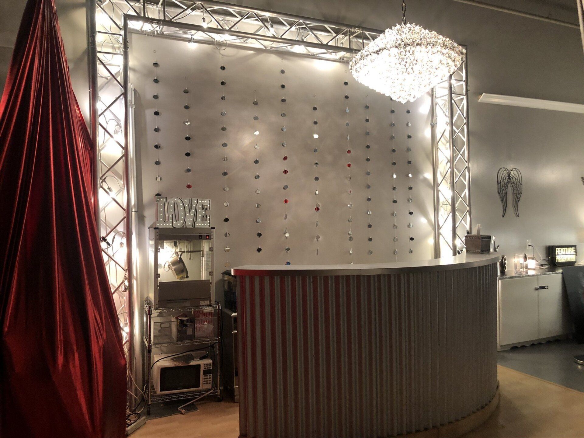 Modern event booth with white studded backdrop, red drape, and curved counter under bright chandelier lights