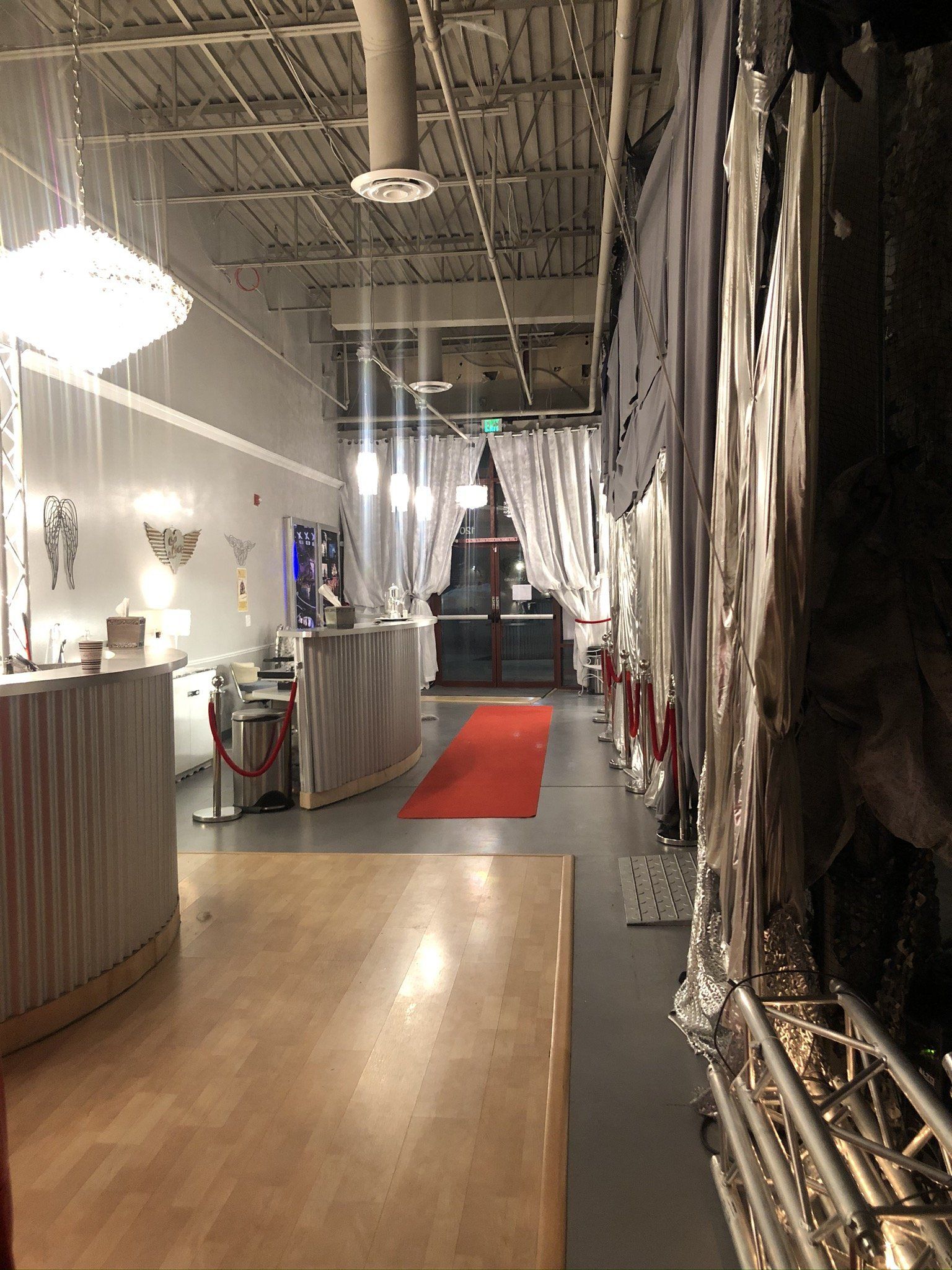 Narrow indoor hallway with red carpet, draped walls, and hanging lights in a decorated event space