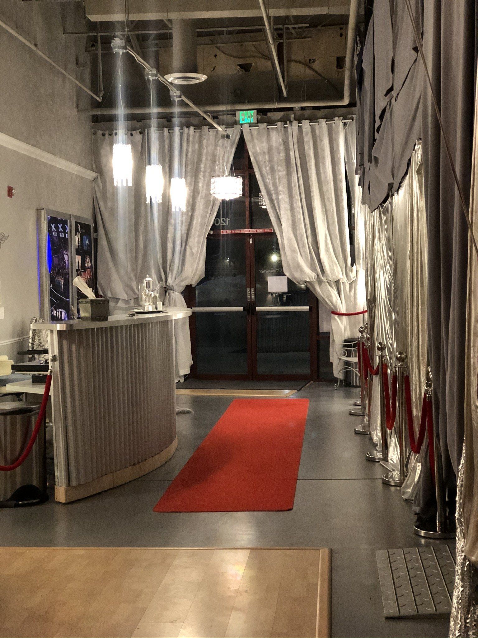 Industrial hallway with a red runner carpet, white curtains, and hanging lights leading to glass doors