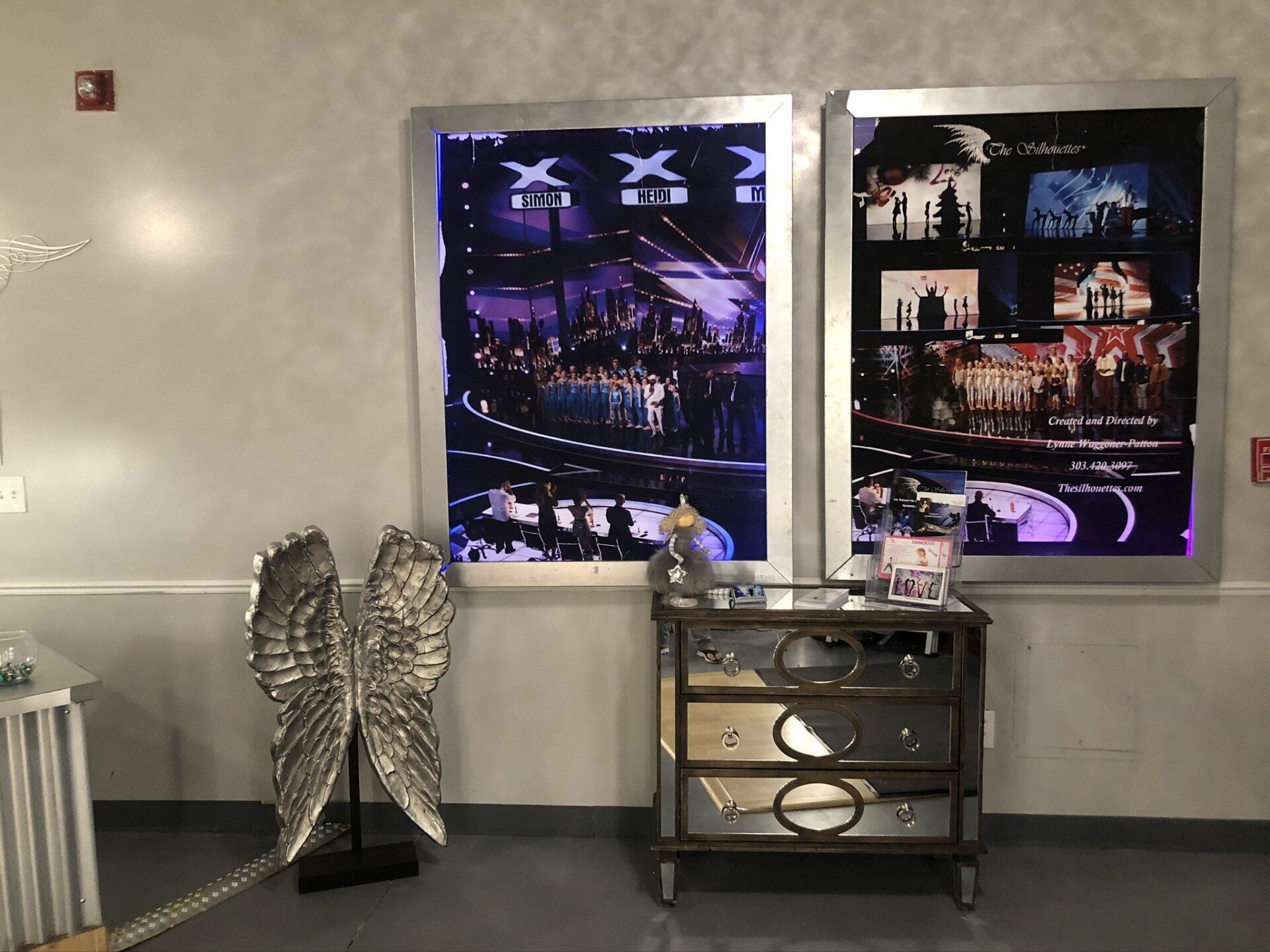 Lobby wall with two large framed posters above a small black cabinet and decorative sculpture.