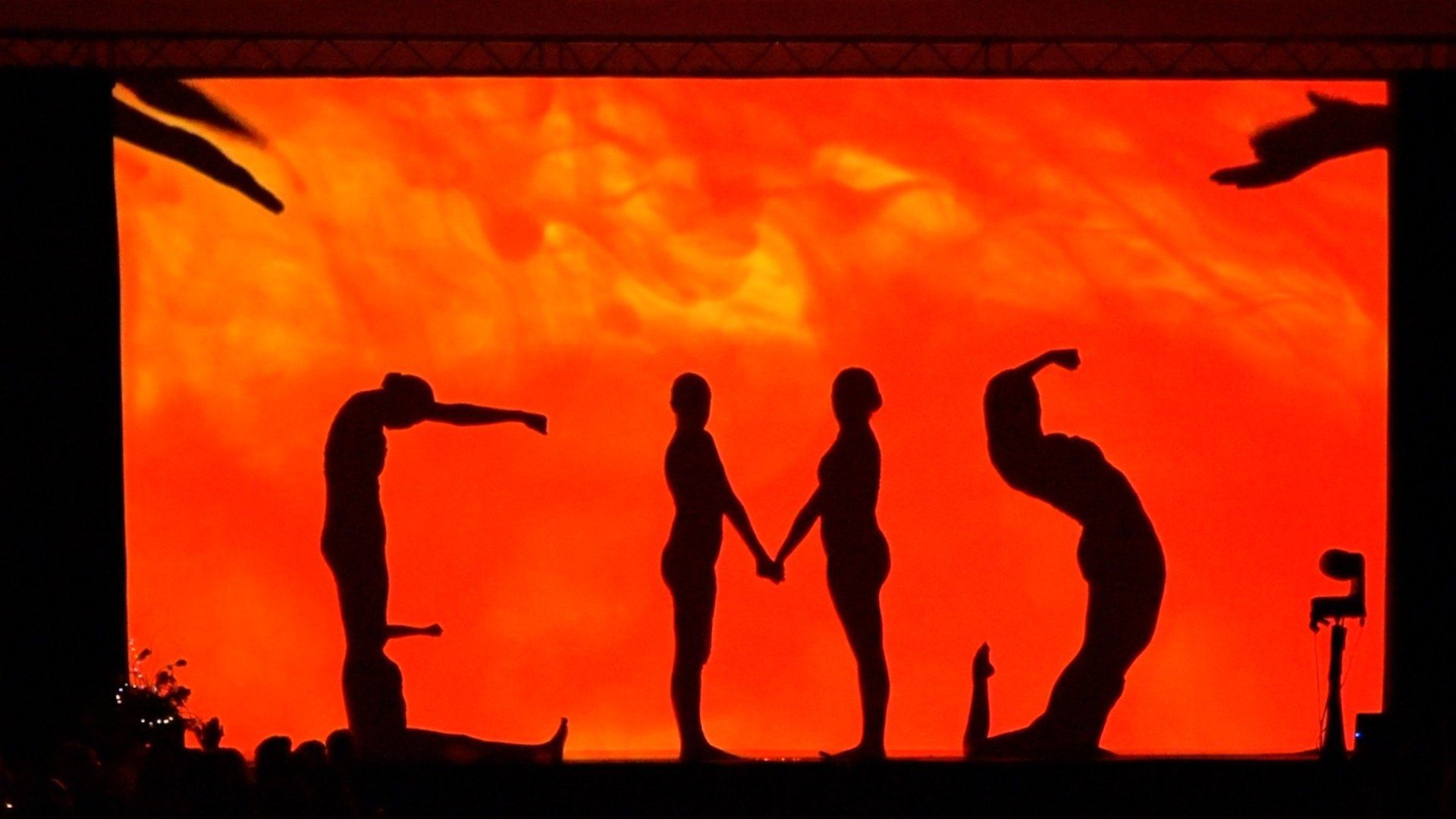 Silhouettes of people holding hands and gesturing against a bright orange sunset sky