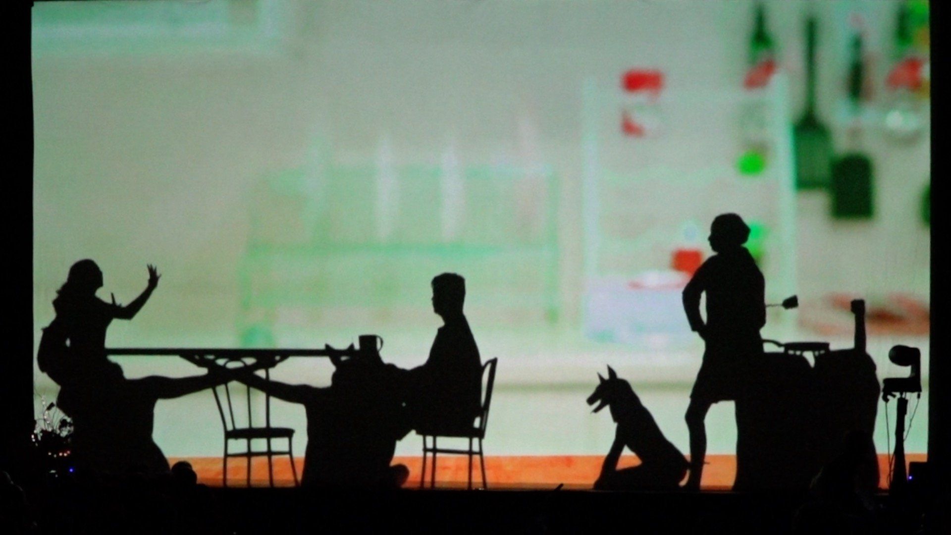 Silhouetted people at tables in a softly lit indoor café or restaurant, with a dog in the foreground.