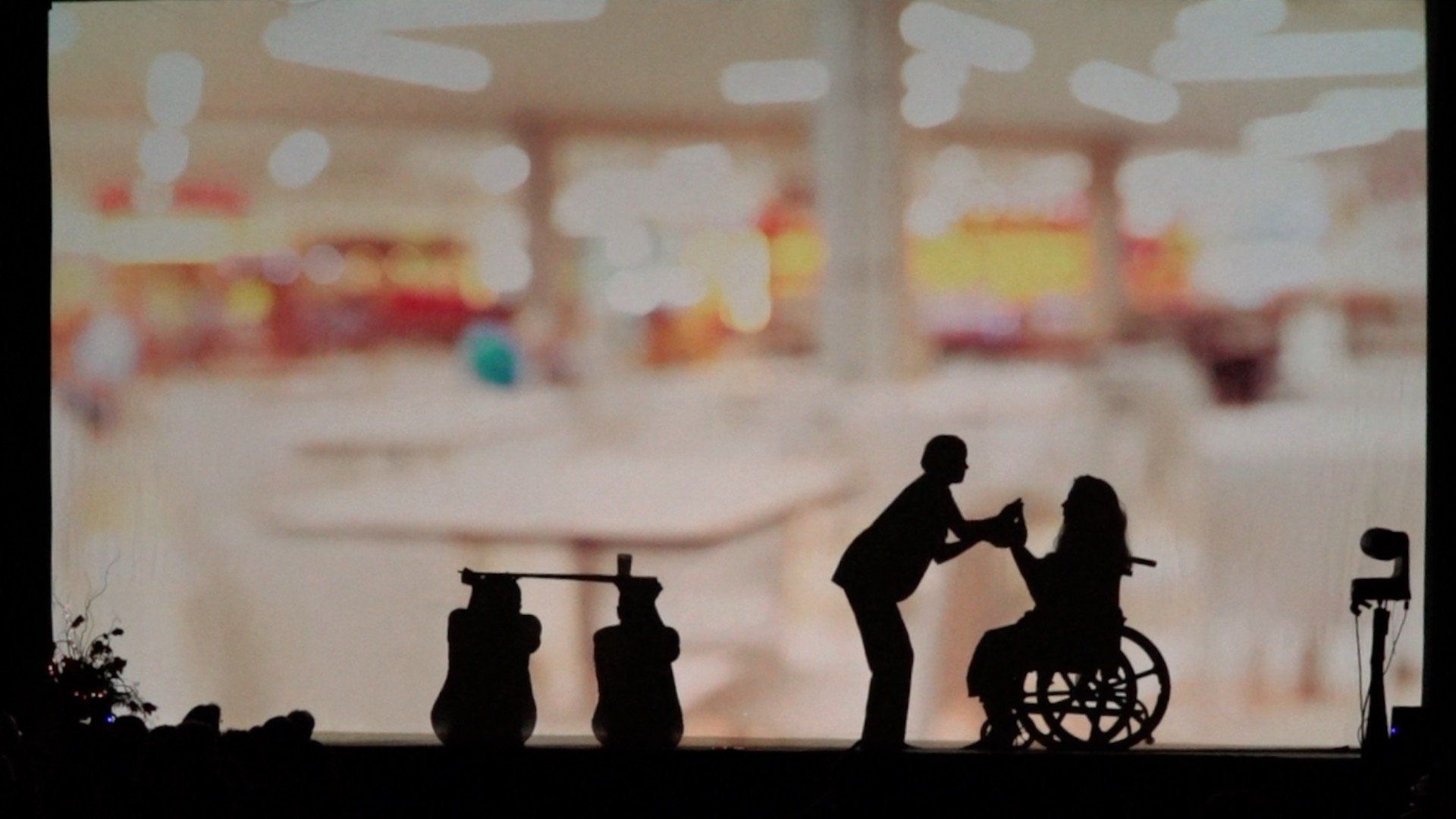 Silhouettes of people in a wheelchair scene at a bright indoor airport or mall