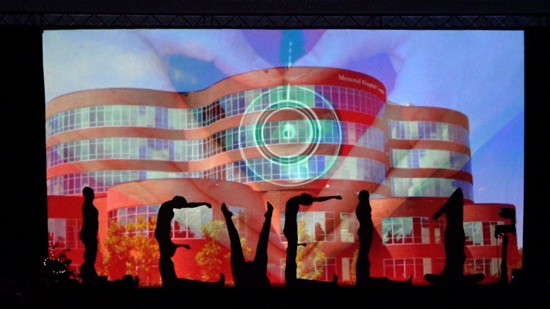 Silhouetted people in front of a glowing red building with a blue circular light projection