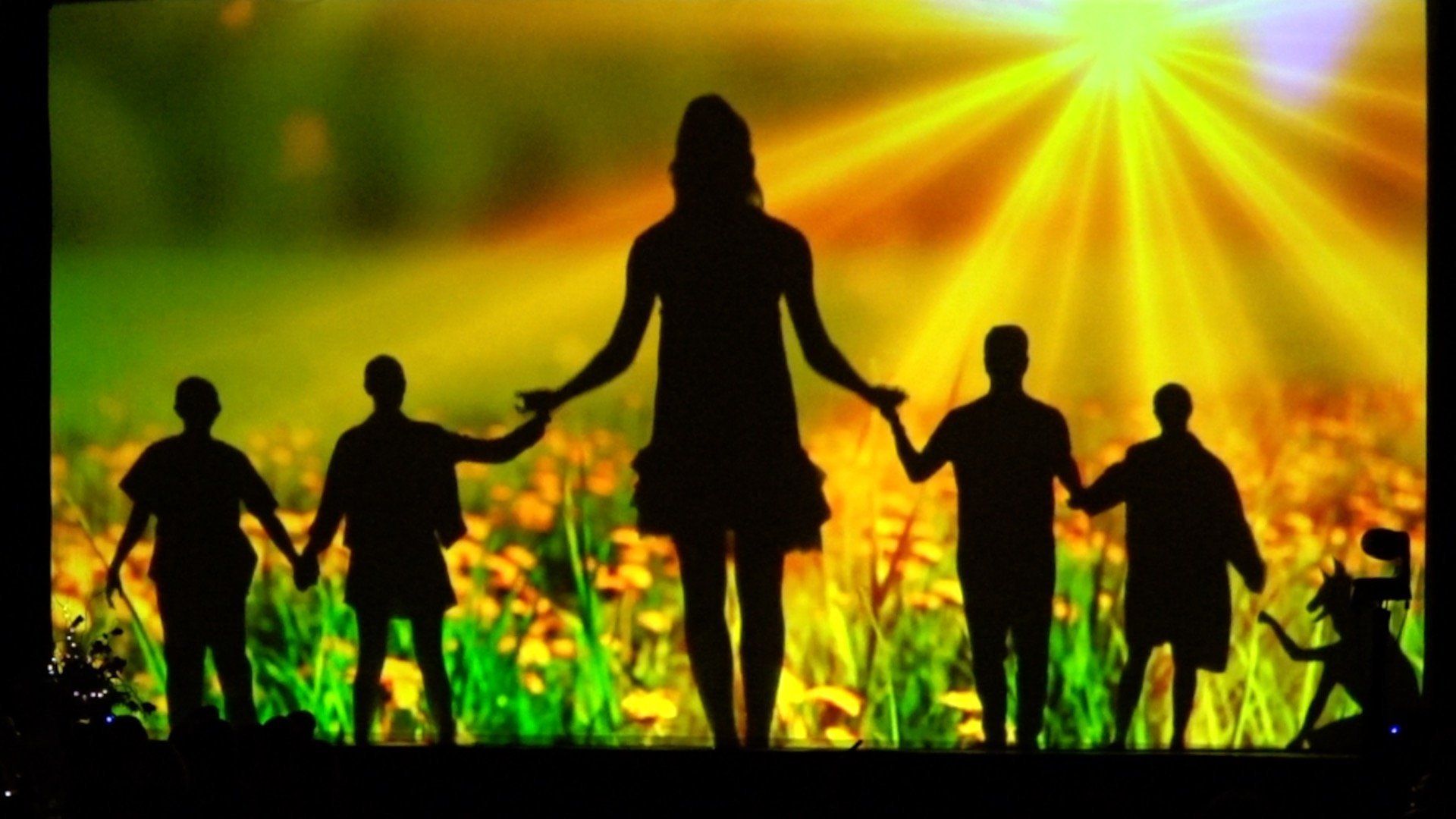 Silhouetted people holding hands in a field under bright golden sunlight