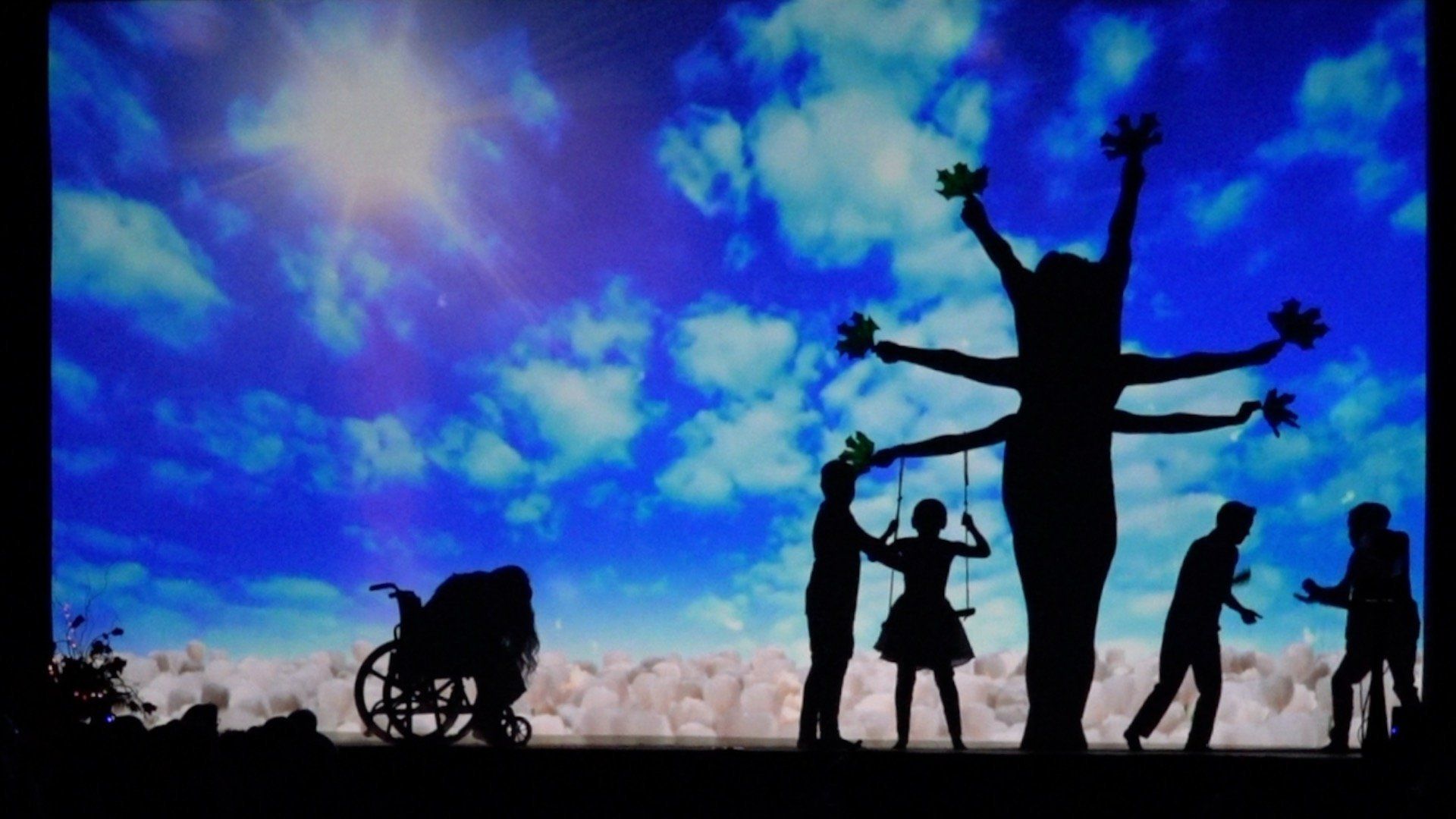 Silhouetted people and a tree against a bright blue, cloudy sky at sunset