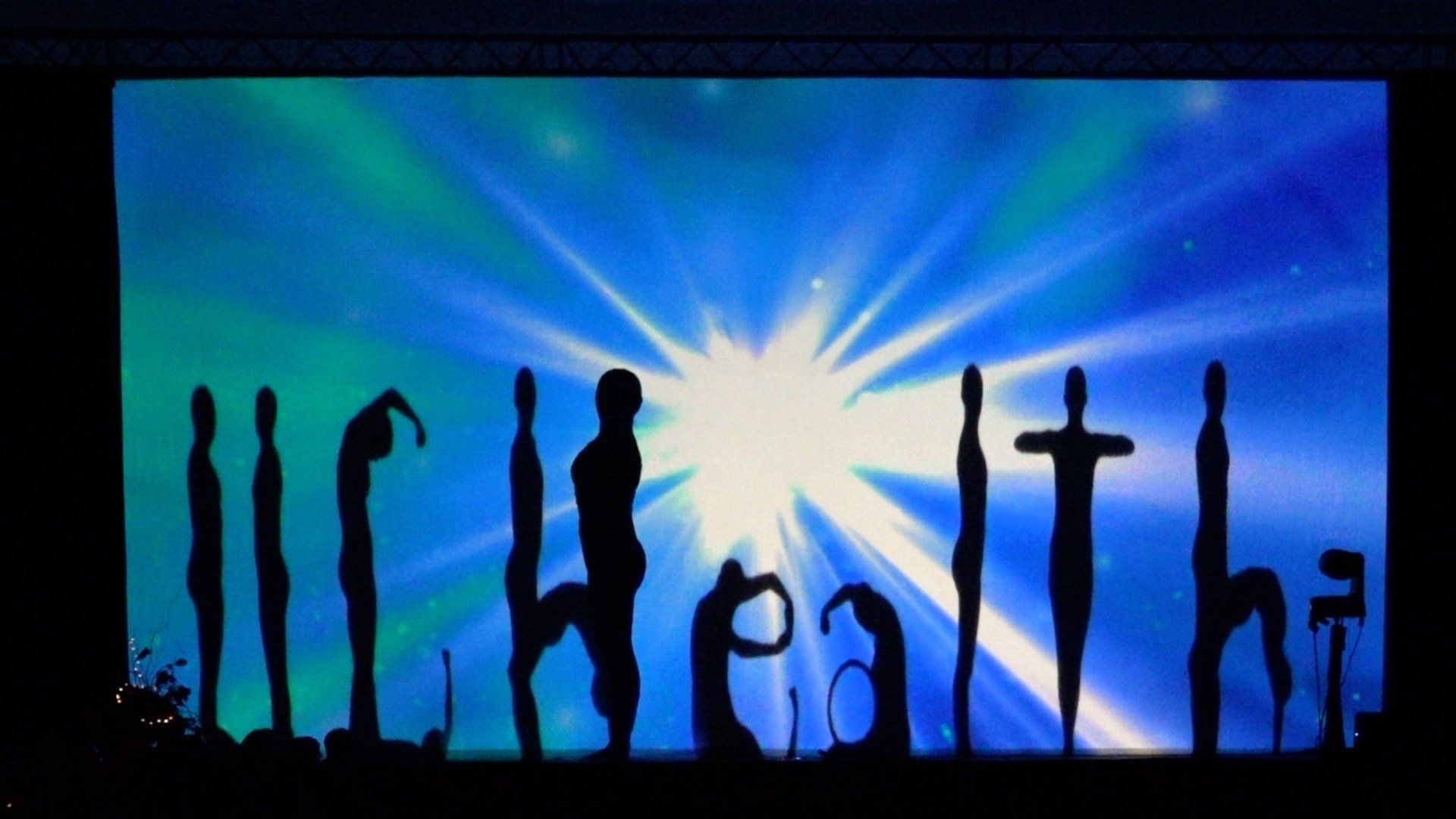 Silhouetted people holding yoga poses against a bright blue sunburst sky, with “health” spelled below