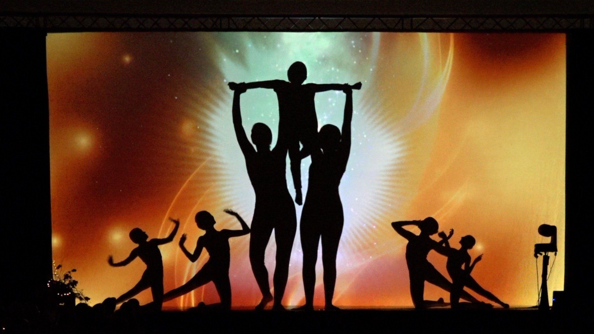 Silhouetted dancers in dramatic poses against a warm orange stage-lit background
