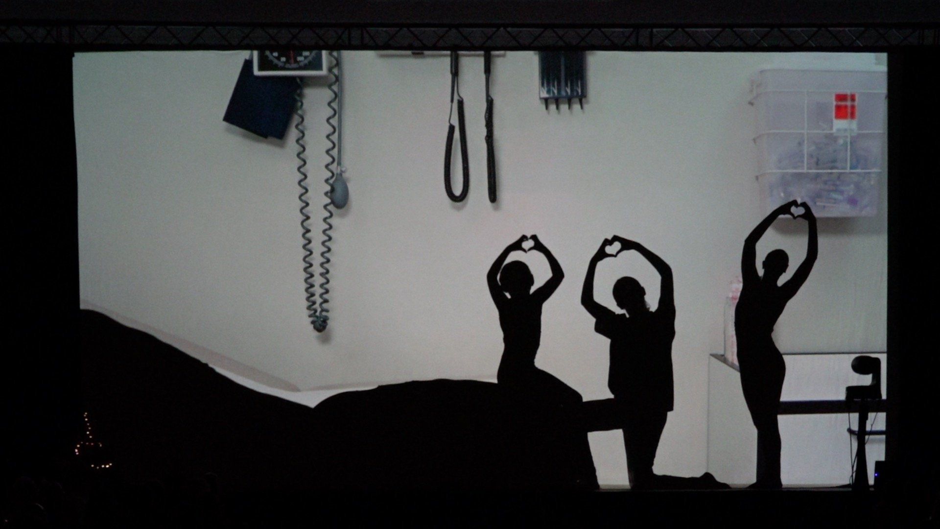 Three silhouetted people stand with arms raised in a gym or studio, with wall equipment behind them.