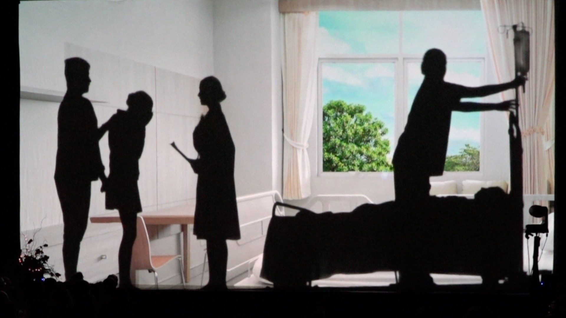 Silhouettes of four people in a room; one reaches to open curtains by a sunlit window.