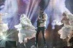 Dancers in white costumes performing on a lit stage with one person centered in black.