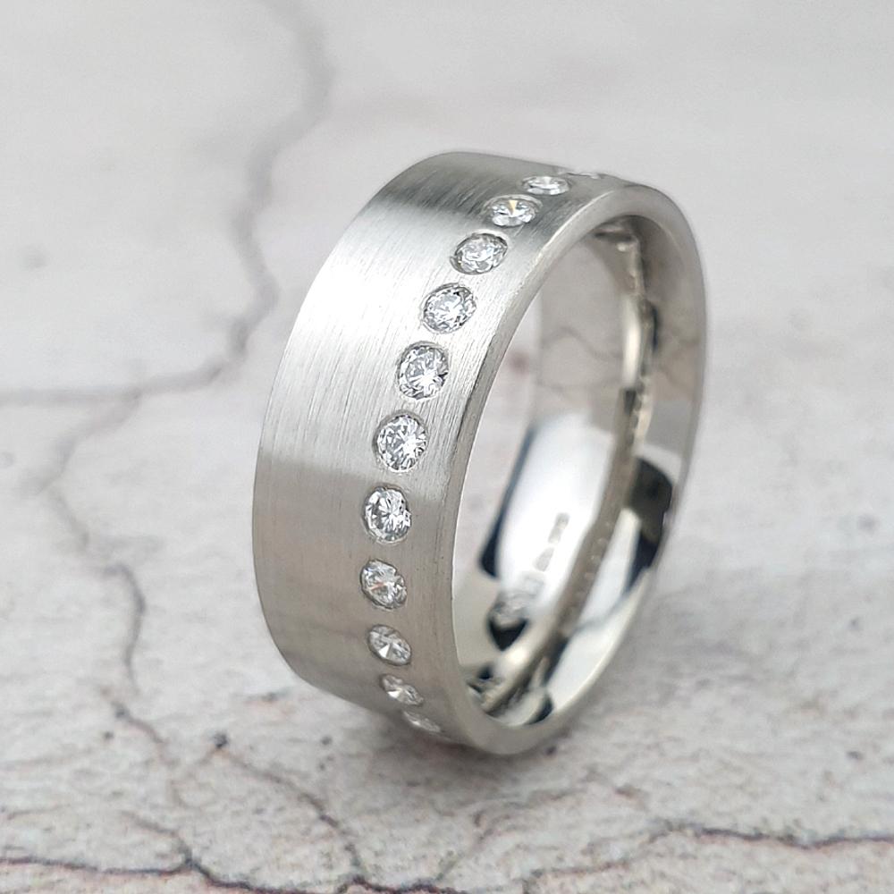 A wide platinum flat-court wedding ring with an off-centre line of diamonds