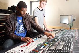 Two people adjusting knobs and sliders on a large audio mixing console in a studio