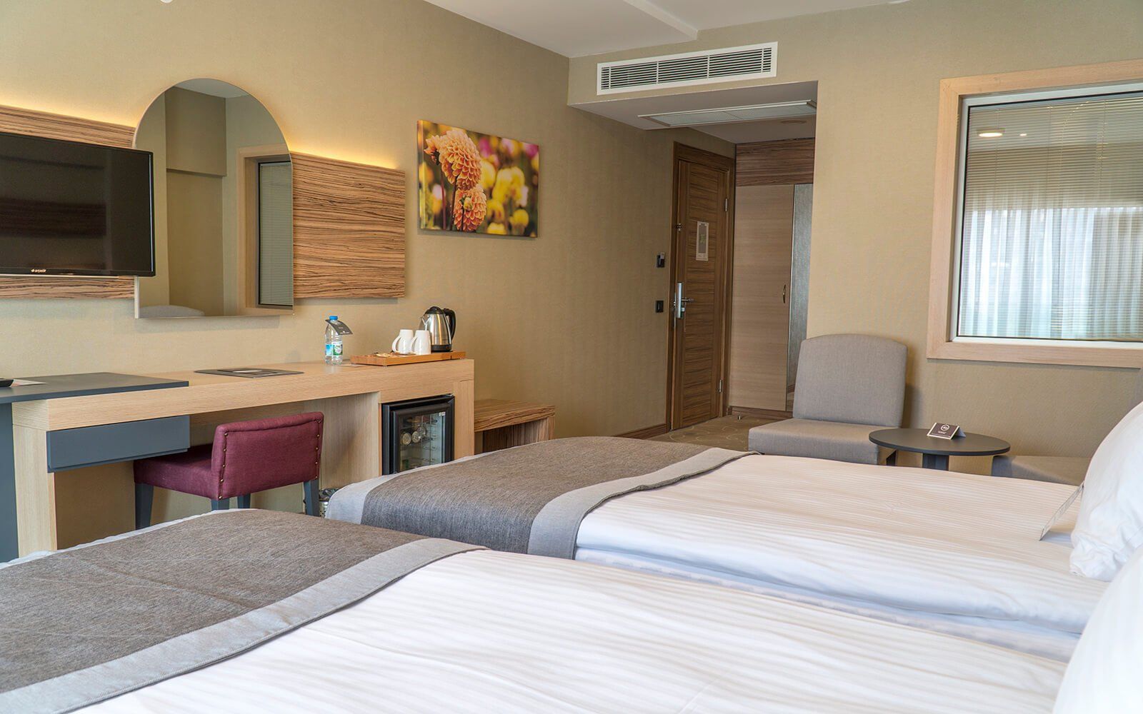 Iki yatak, bir masa, bir sandalye ve bir televizyonun bulunduğu bir otel odası.