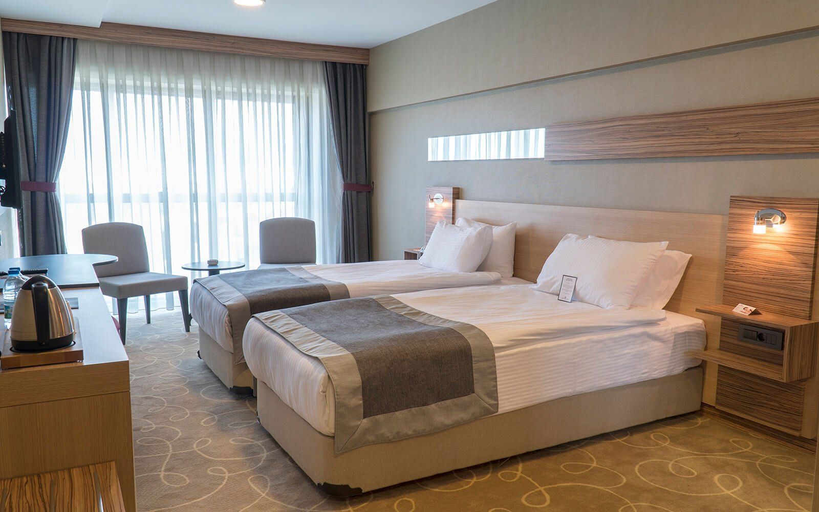 Iki yatak, bir masa, sandalyeler ve bir pencere bulunan bir otel odası.