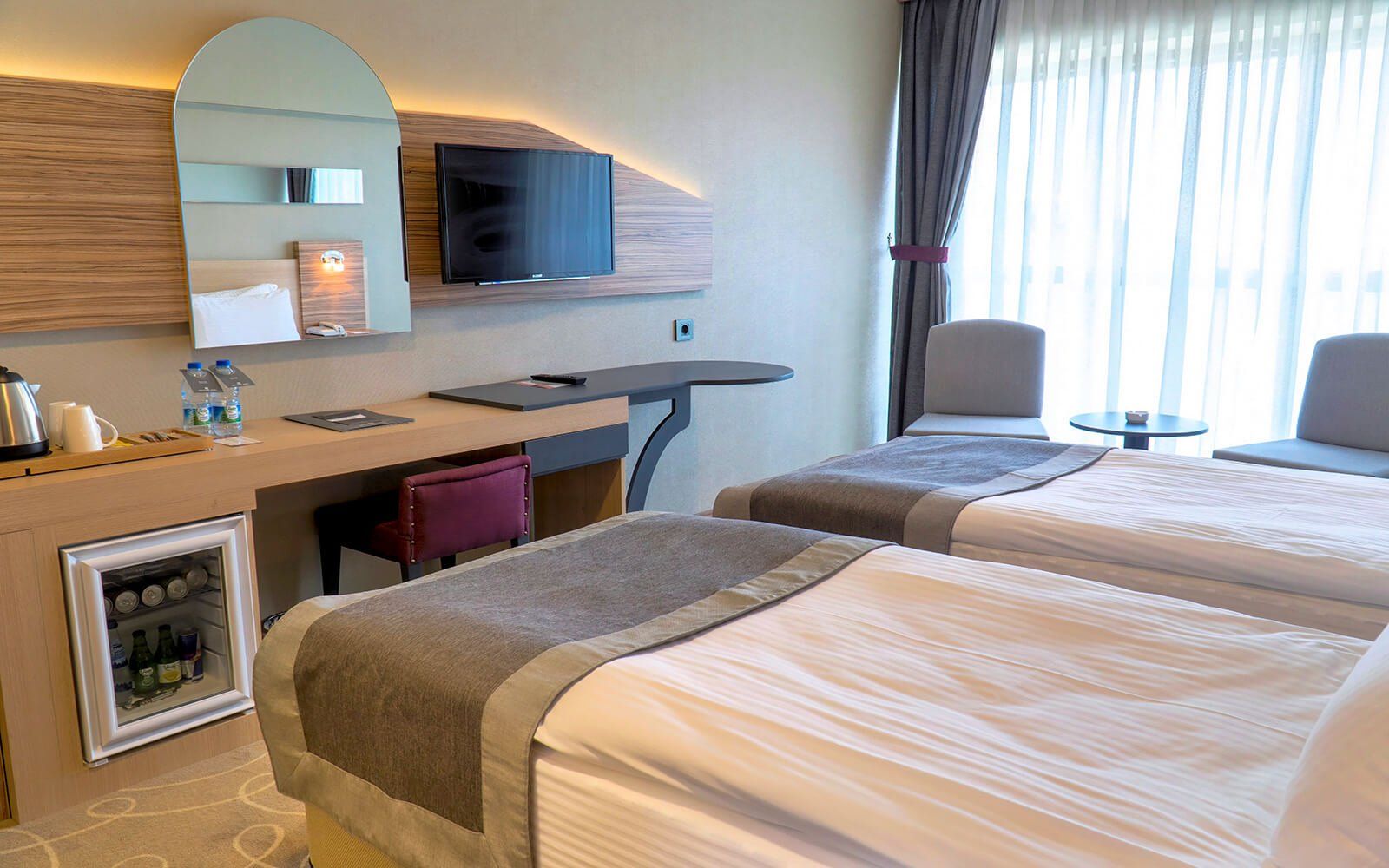 Iki yatak, bir masa, sandalyeler ve bir buzdolabı bulunan bir otel odası.