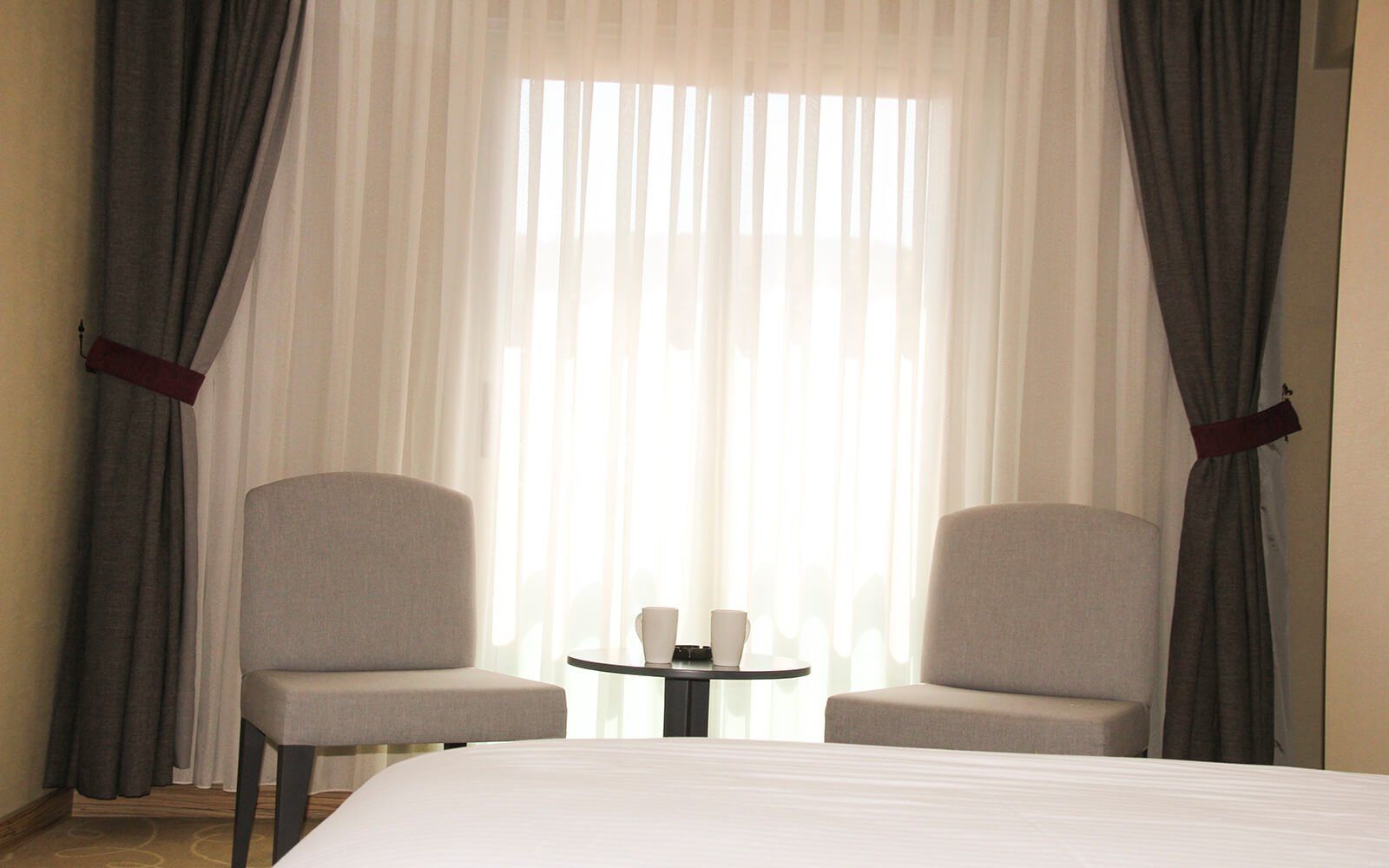Büyük bir pencerenin önünde iki sandalye ve bir masa bulunan bir otel odası.
