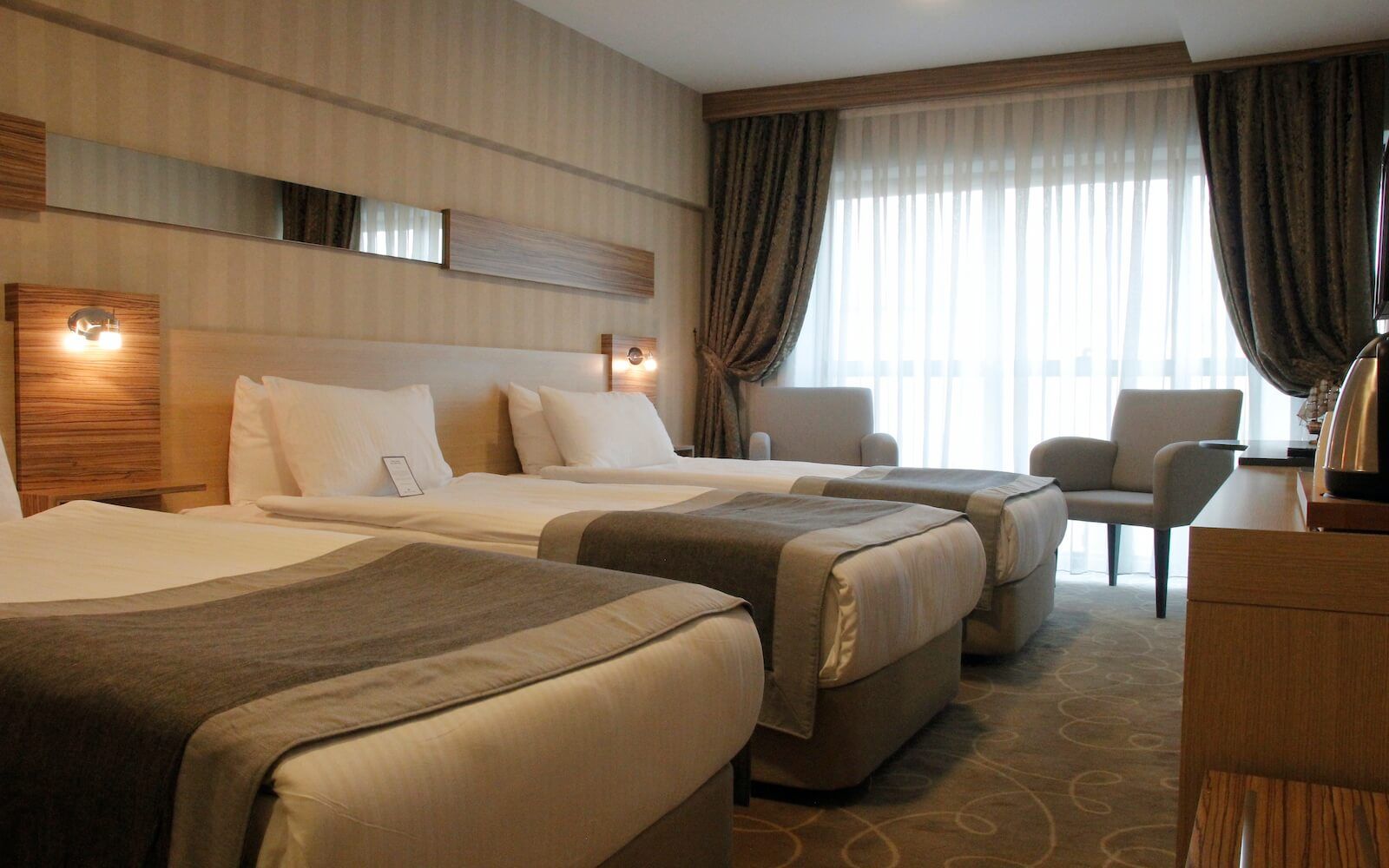 Üç yataklı ve geniş pencereli bir otel odası.