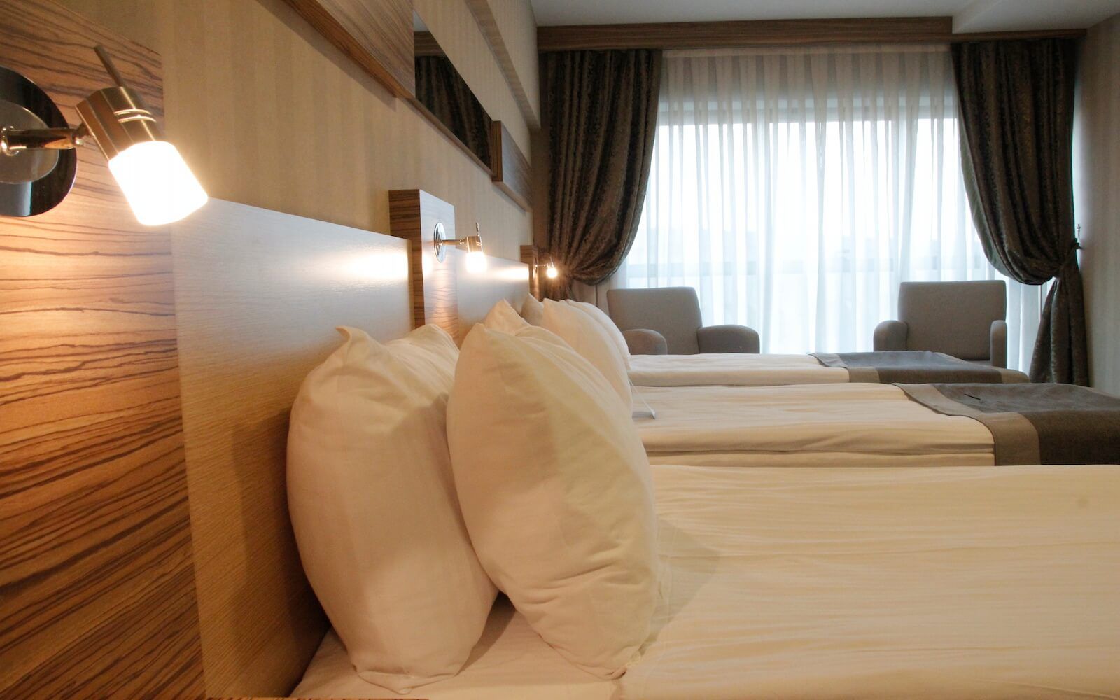 Üç yataklı ve geniş pencereli bir otel odası.