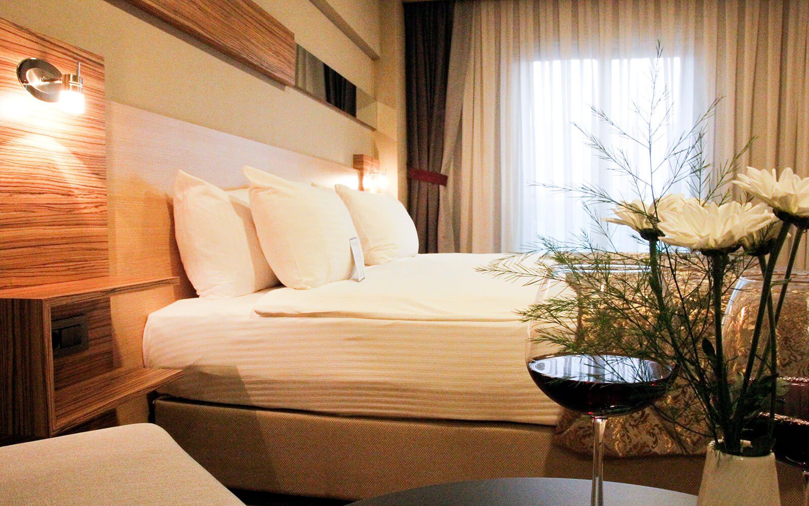 Bir yatak ve bir kadeh şarap bulunan bir otel odası
