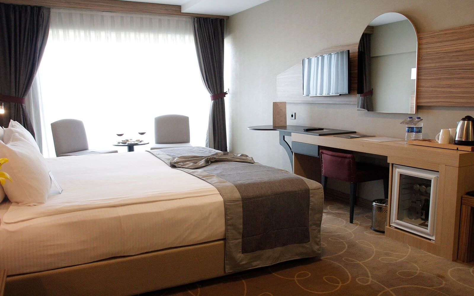Yatak, çalışma masası, sandalyeler ve televizyonun bulunduğu bir otel odası.