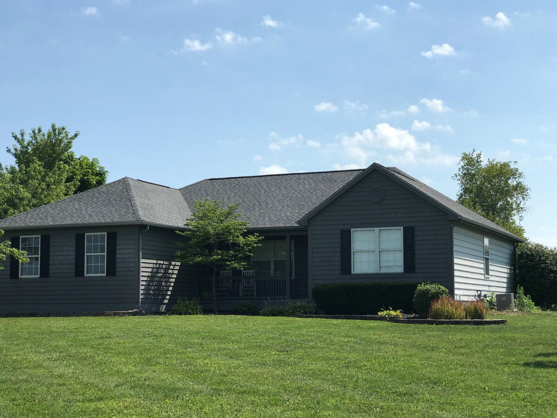 Gray-sided house with black shutters and roof on a green lawn under a blue sky.
