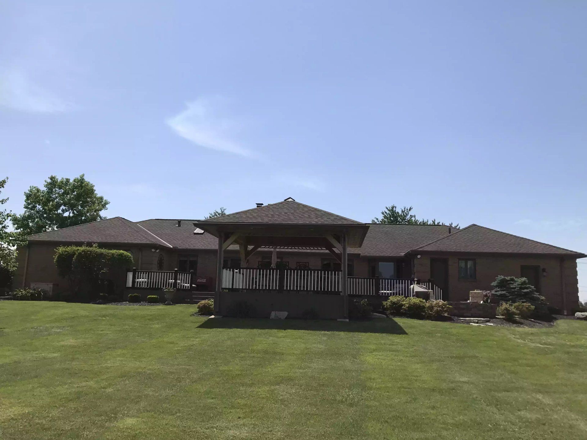 Gazebo on a green lawn in front of a brick house with a blue sky background.