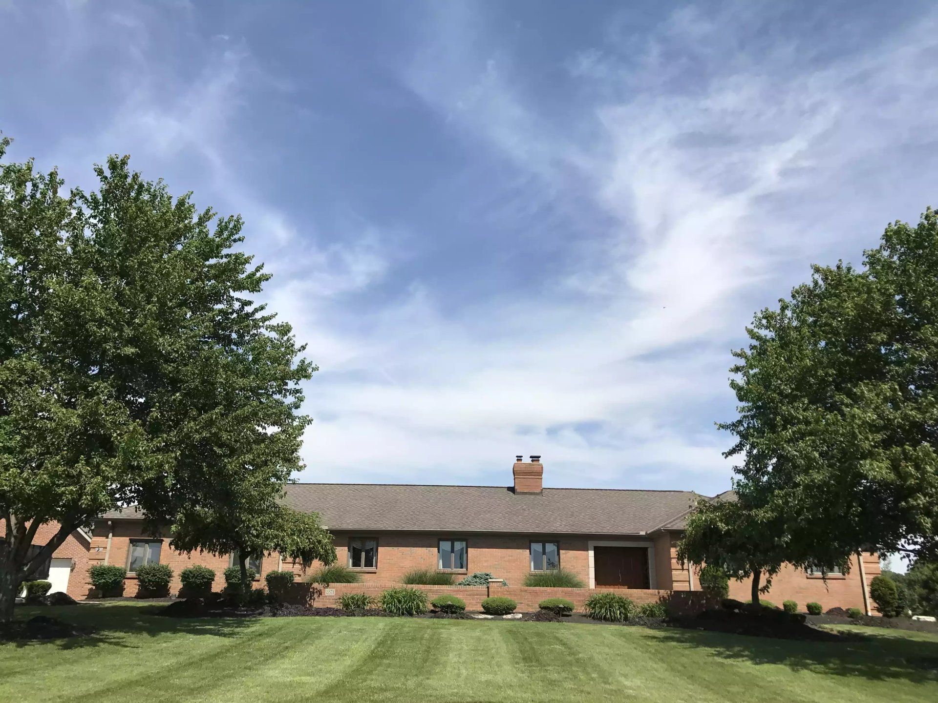 A brick building with trees on either side, centered under a blue sky with streaky clouds.