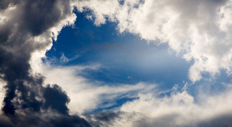 The sun is shining through the clouds in the blue sky.
