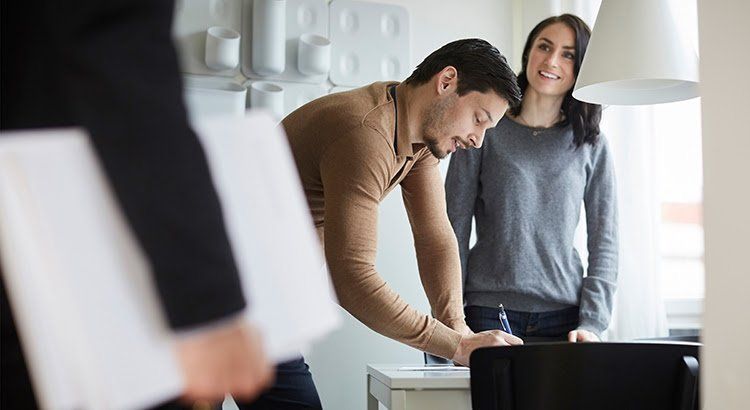 A man and a woman are signing a document in a kitchen.