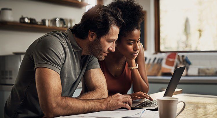 A man and a woman are sitting at a table looking at a laptop.