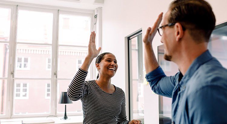 A man and a woman are giving each other a high five in an office.