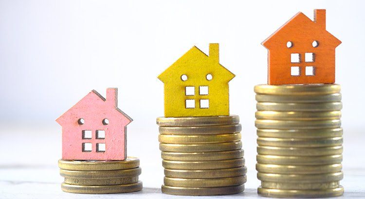 Three wooden houses are sitting on top of stacks of coins.