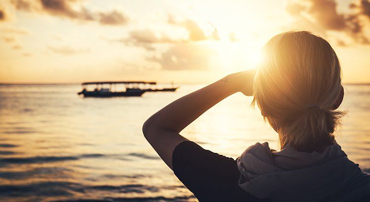 A woman is looking at a boat in the ocean at sunset.